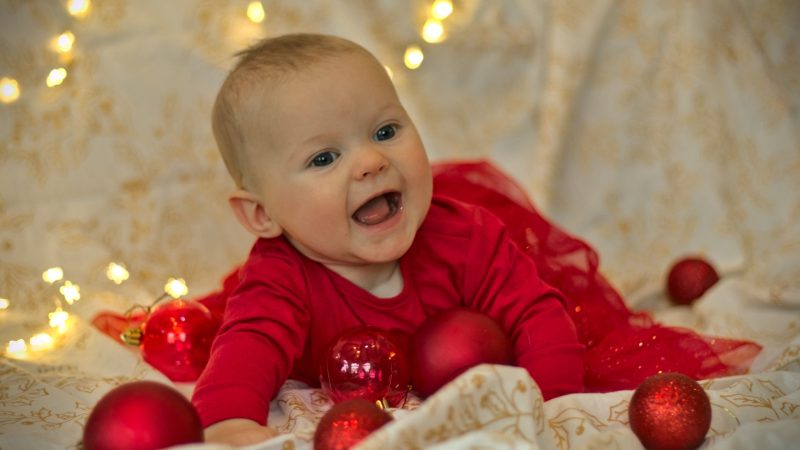 Kleinkind in rotem Kleid spielt mit Christbaumkugeln